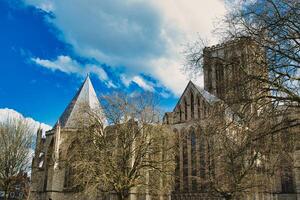 Historic medieval cathedral with Gothic architecture, featuring pointed arches and robust stone walls, set against a vibrant blue sky with fluffy clouds in York, North Yorkshire, England. photo