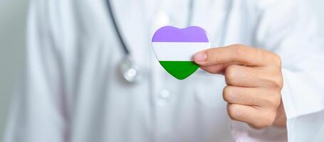 Queer Pride Day and LGBT pride month concept. Doctor hand holding purple, white and green heart shape with Stethoscope for Lesbian, Gay, Bisexual, Transgender, genderqueer and Pansexual community photo