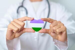 Queer Pride Day and LGBT pride month concept. Doctor hand holding purple, white and green heart shape with Stethoscope for Lesbian, Gay, Bisexual, Transgender, genderqueer and Pansexual community photo