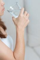 Happy woman holding water glass, female drinking pure water on sofa at home. Healthy, Refreshment, lifestyle and daily routine concept photo