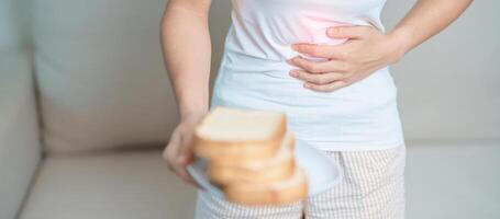 gluten intolerancia, gluten gratis y celíaco enfermedad o trigo alergia concepto. mujer sostener un pan y teniendo abdominal dolor después comer gluten. estómago dolor, náuseas, hinchazón, gas, Diarrea y piel erupción foto