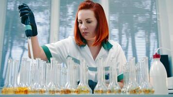 professionell forskare utför kemisk analys i laboratorium. kvinna labb arbetstagare försiktigt använder sig av dropper till fylla flera olika testa rör med exakt belopp av gul flytande video