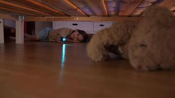 un' poco ragazza è guardare per sua preferito giocattolo sotto il letto con un' torcia elettrica video