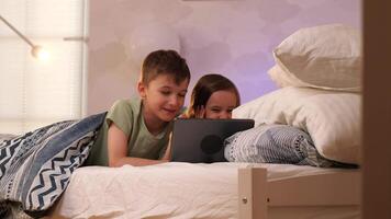 Garoto e menina assistindo em tábua antes indo para cama deitado dentro cama video