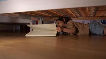 un pequeño niña debajo el cama mira a un libro, propio mundo de un pequeño niño video