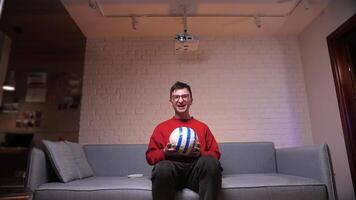 a football fan in red clothes in front of the screen watches the game, video