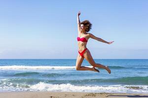 Slim woman in bikini jumping on sandy beach photo