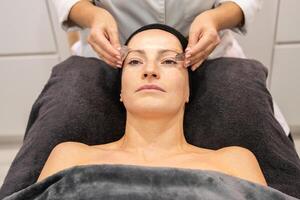 Woman receiving facial skin treatment from crop masseuse in beauty center photo