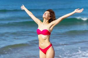 Happy slim woman in bikini with raised arms photo