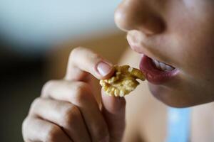 Crop anonymous teenage girl eating healthy walnut kernel photo