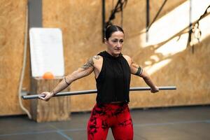 Strong tattooed woman stretching with a bar in a gym photo