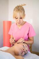 Professional beautician applying ear probe on female client in salon during auriculotherapy photo