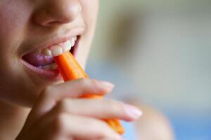 Unrecognizable girl eating fresh carrot slice at home photo