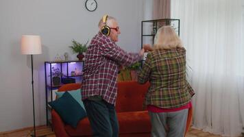 Happy senior grandparents man woman listening music dancing disco fooling around having fun at home video