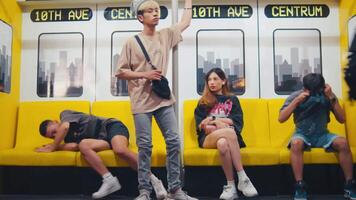 Passengers in a subway train with a young man standing and others seated, absorbed in their phones, with a cityscape in the background. video