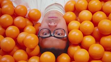 Person submerged in a pool of orange balls, wearing glasses, with only their face visible, creating a quirky and playful image. video