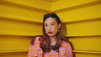 Stylish woman in floral dress posing against yellow staircase, exuding confidence and retro fashion vibes. video