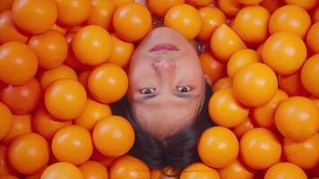 Person submerged in a sea of bright orange balls, with only their face visible, creating a playful and vibrant image. video