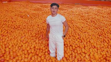 Man standing amidst a sea of oranges, expressing surprise or overwhelm. video