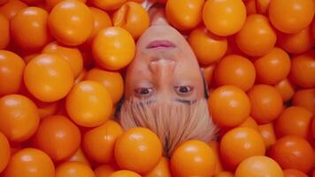 Creative portrait of a person submerged in bright orange balls, with only their face visible, conveying a sense of playfulness and abstraction. video