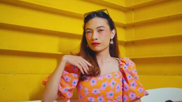 Stylish woman with sunglasses on head posing against yellow background, hand extended as if to show stop gesture. video