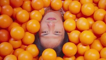 Close-up of a person's face surrounded by bright orange balls, creating a playful and vibrant background. video