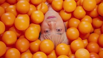 Creative portrait of a person submerged in bright orange balls, with only their face visible, conveying a playful and abstract concept. video