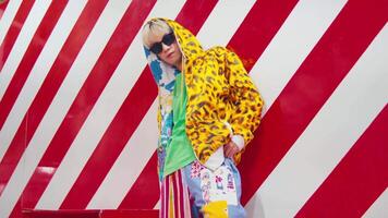 Stylish person posing against a red and white striped background, wearing colorful, trendy outfit with sunglasses. video