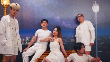 Group of stylish young people posing in white outfits against a starry night backdrop with a streetlamp and bench. video