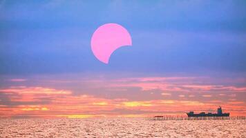 solar eclipse vermelho pôr do sol em a oceano com carga navio e vermelho laranja amarelo nuvem fundo Tempo lapso video