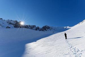 A mountaineer walking on the mountains. Beautiful sunny day for outdoor winter hike. Winter traveling. Adventure. Scenic view. photo