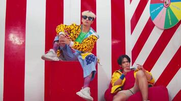 Stylish young couple in colorful outfits posing in a vibrant retro setting with geometric patterns and a wheel of fortune. video