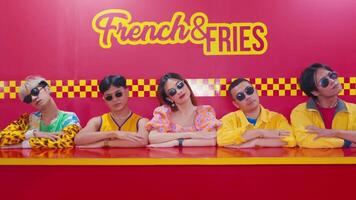 elegante joven personas vistiendo Gafas de sol posando en frente de un vibrante francés y papas fritas neón signo. video