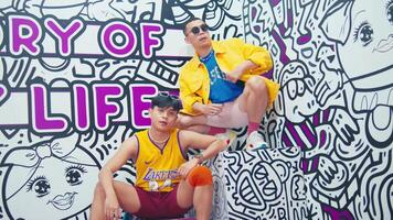 Two young men posing in front of a colorful graffiti wall with the text Story of Life in a playful, urban setting. video