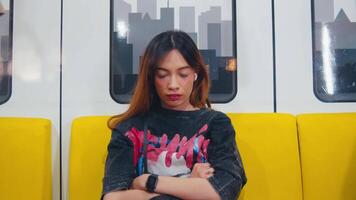 Thoughtful young woman sitting on a yellow subway seat with city silhouette in the background. video