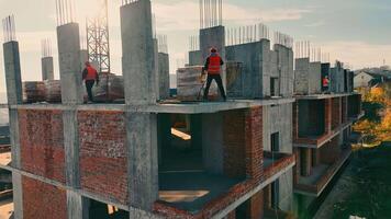 construcción de de muchos pisos residencial edificio desde monolito y ladrillos varios obreros en chalecos y sombreros duros desempacar edificio materiales en construcción sitio video