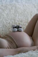 Pregnant woman holding baby booties on her belly, close up photo