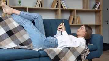 sorridente bellissimo ragazza rilassante su un' divano a casa, utilizzando mobile Telefono video