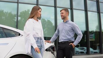 Young couple man and woman traveling together by new car having stop at charging station video