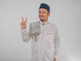 Moslem Asian man smiling at the camera and showing two fingers photo