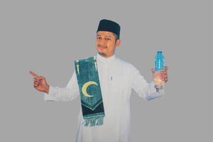 musulmán hombre sonriente mientras participación un botella de Bebiendo agua y señalando a el Derecha lado foto