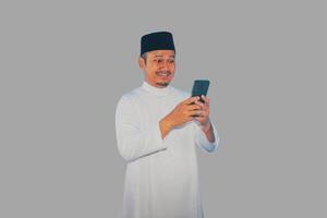 Moslem Asian man smiling happy when texting using his mobile phone photo