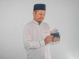 Side view of Moslem Asian man smiling happy when taking money from inside his wallet photo