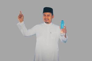 Moslem man smiling while holding a bottle of drinking water and pointing to the right top side photo