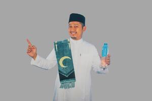 Moslem man smiling while holding a bottle of drinking water and pointing to the right side photo