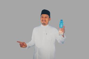 Moslem man smiling while holding a bottle of drinking water and pointing to the right side photo