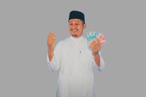 asiático musulmán hombre demostración contento expresión mientras participación dinero foto