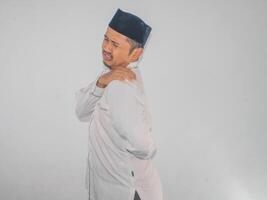 Asian muslim adult man touching his left shoulder with painful expression photo