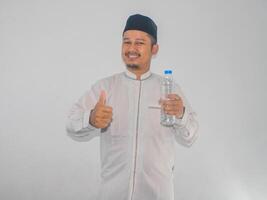 Moslem man smiling while holding a bottle of drinking water and give thumb up photo