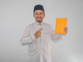 Moslem Asian man smiling while pointing to a book that he hold photo